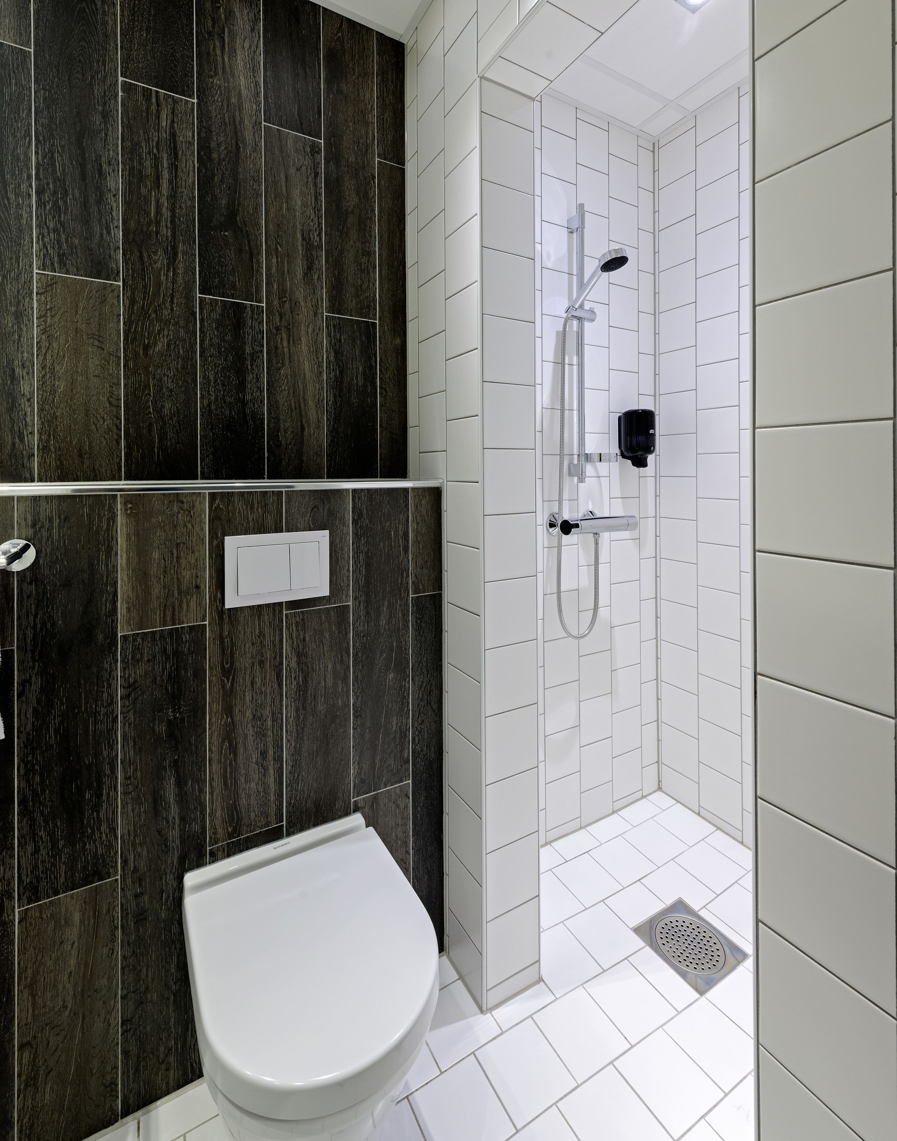 A modern bathroom with a shower, toilet, and dark wood paneling.
