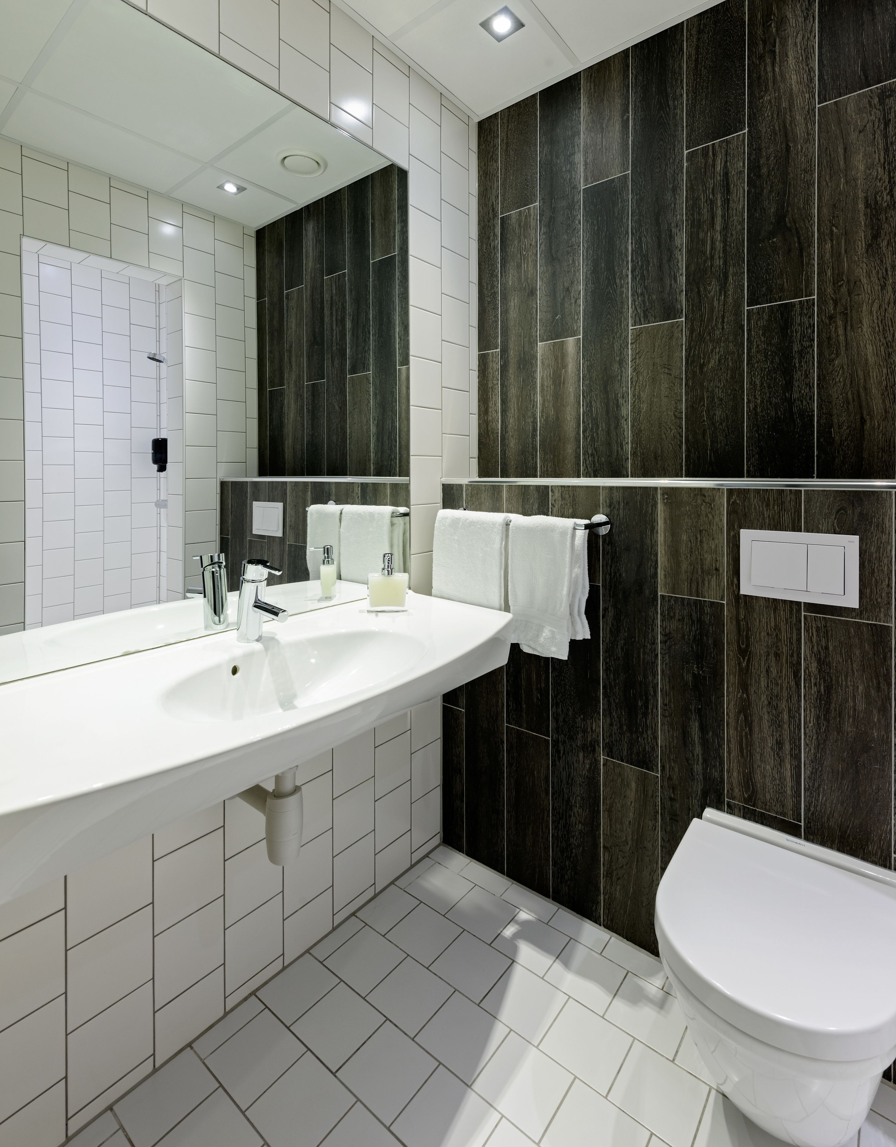 Une salle de bain moderne avec un grand lavabo blanc, des toilettes et un lambris en bois foncé sur les murs.