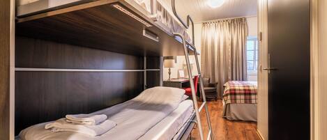 A bunk bed room with a desk and chair, a window with curtains, and a door.