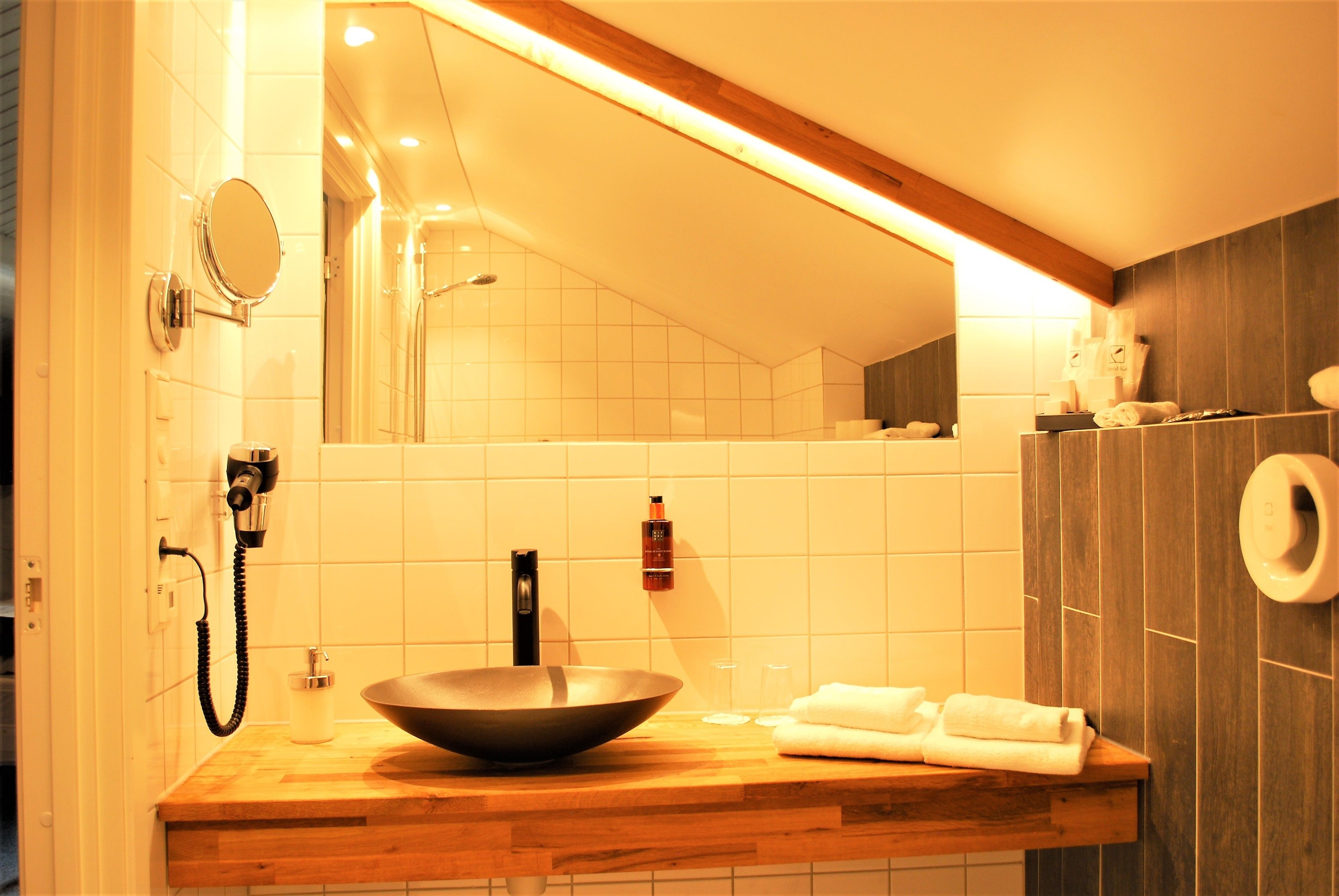 A modern bathroom with a wooden vanity, a large mirror, a vessel sink, and a towel rack.