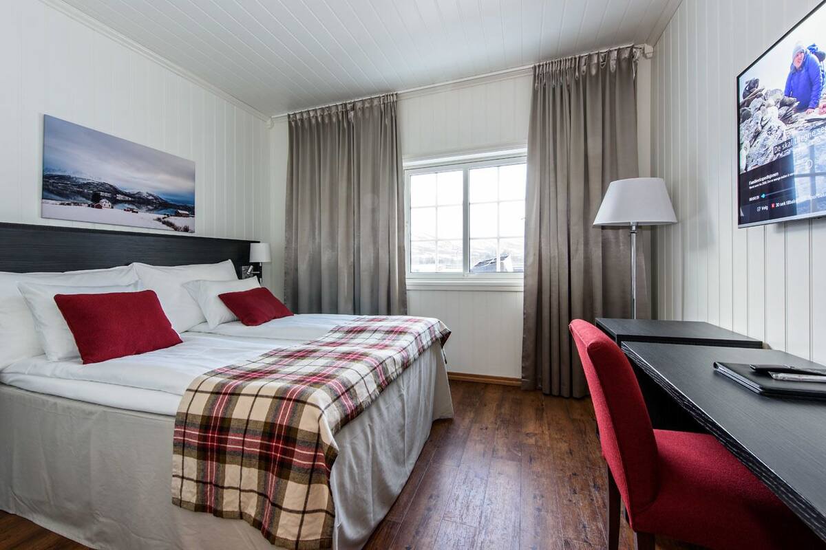 Ein Hotelzimmer mit Bett, Schreibtisch, Stuhl, Fenster und einem Bild an der Wand.
