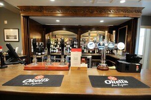 Zona de bar con dos paneles de grifo marcados con “O'reilly's” y una variedad de botellas y vasos al fondo.