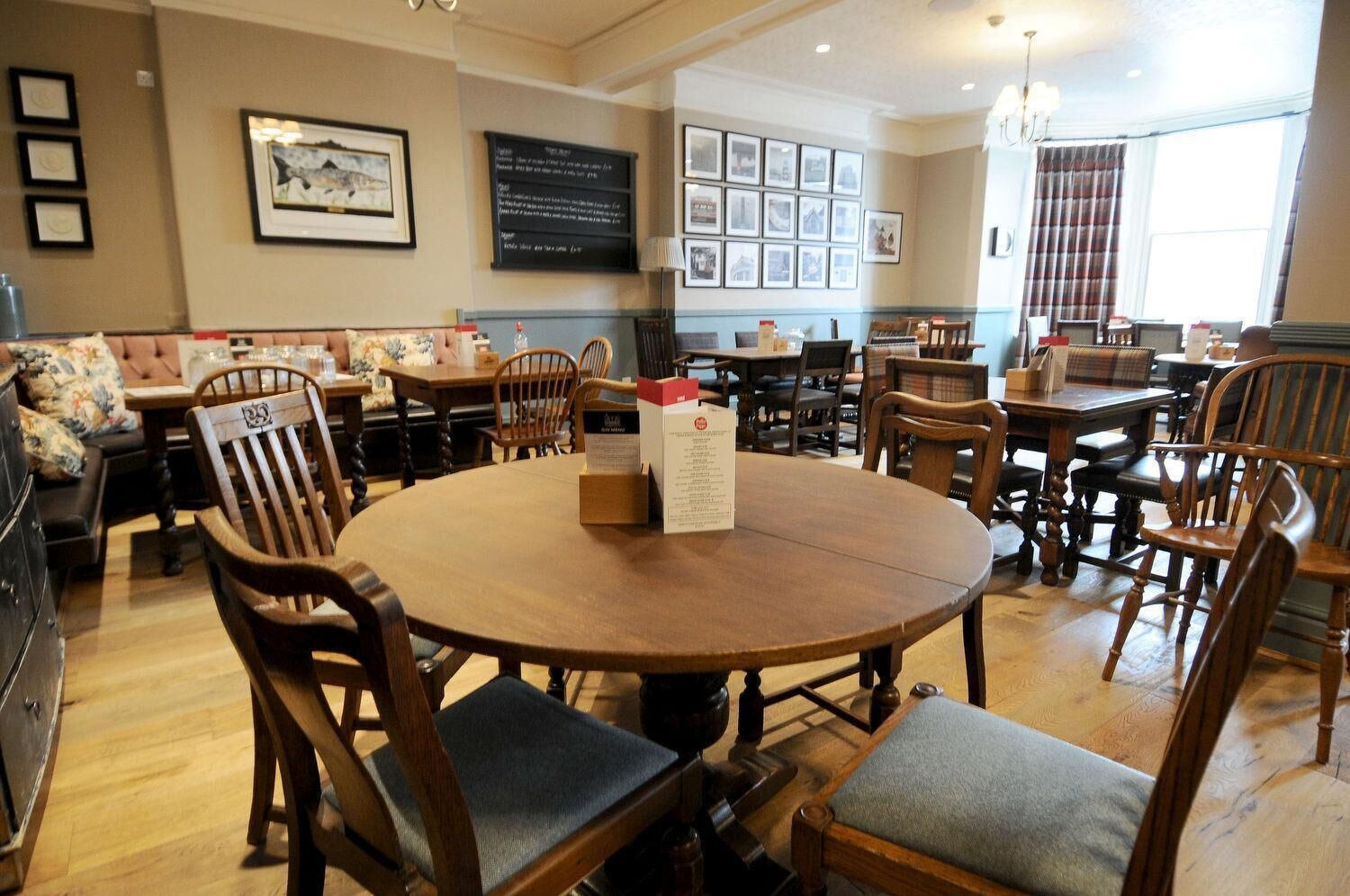 A dining area with wooden tables and chairs, framed pictures on the walls, and a menu stand.