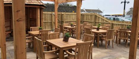 An outdoor patio area with wooden tables and chairs, surrounded by a wooden fence.