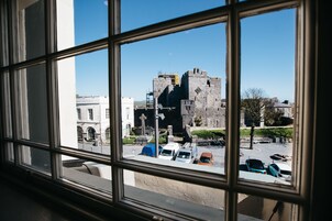 Vista a través de una ventana de una estructura similar a un castillo, con un estacionamiento frente a ella.