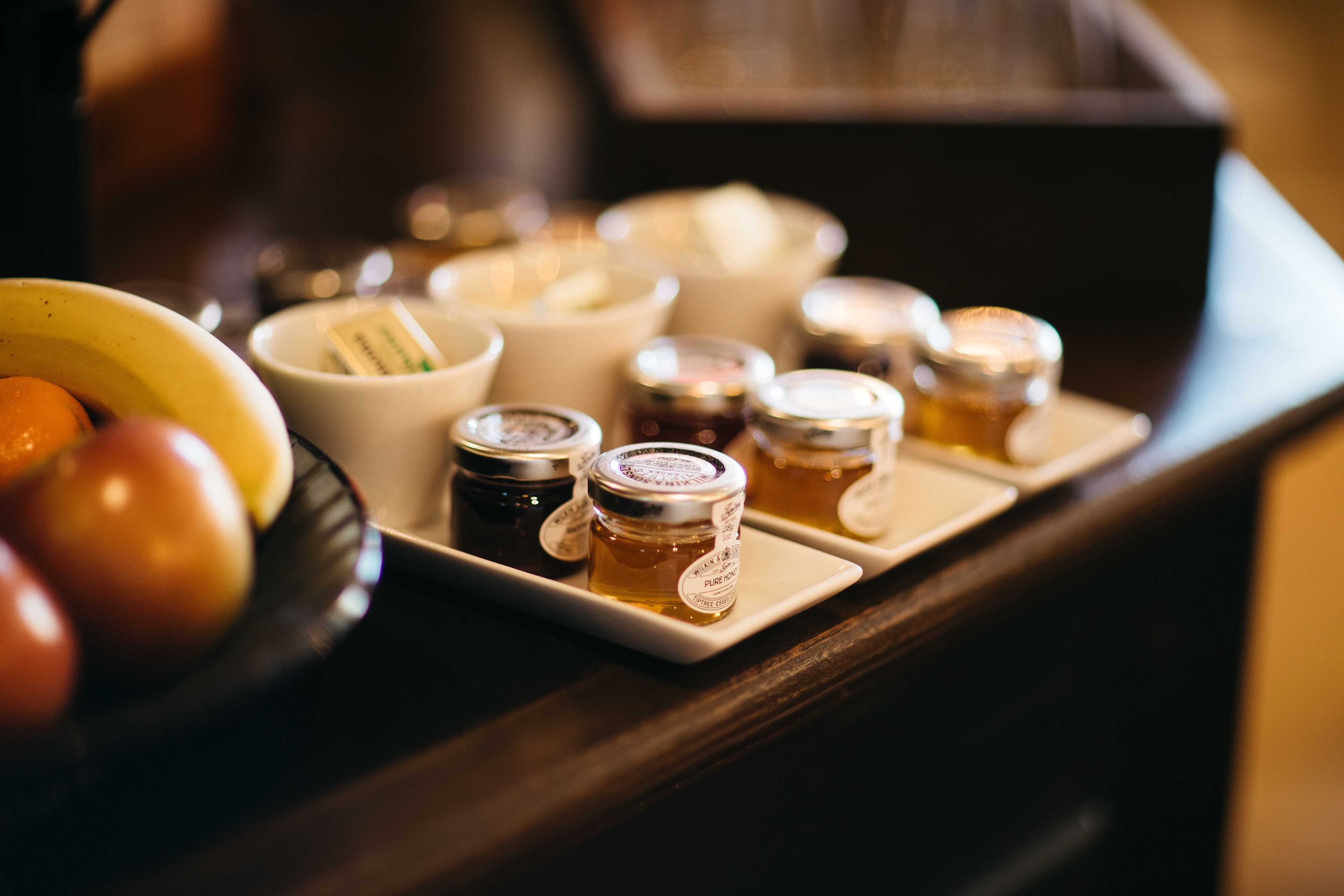 A tray of honey jars and a bowl of fruit on a wooden table.