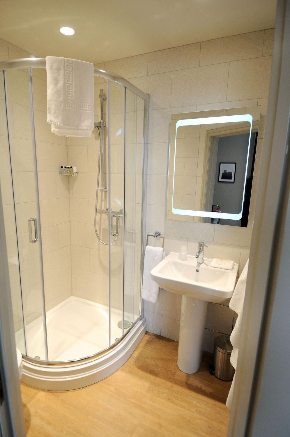 Een moderne badkamer met een douchecabine van glas, een witte wastafel en een spiegel met verlichting rondom.