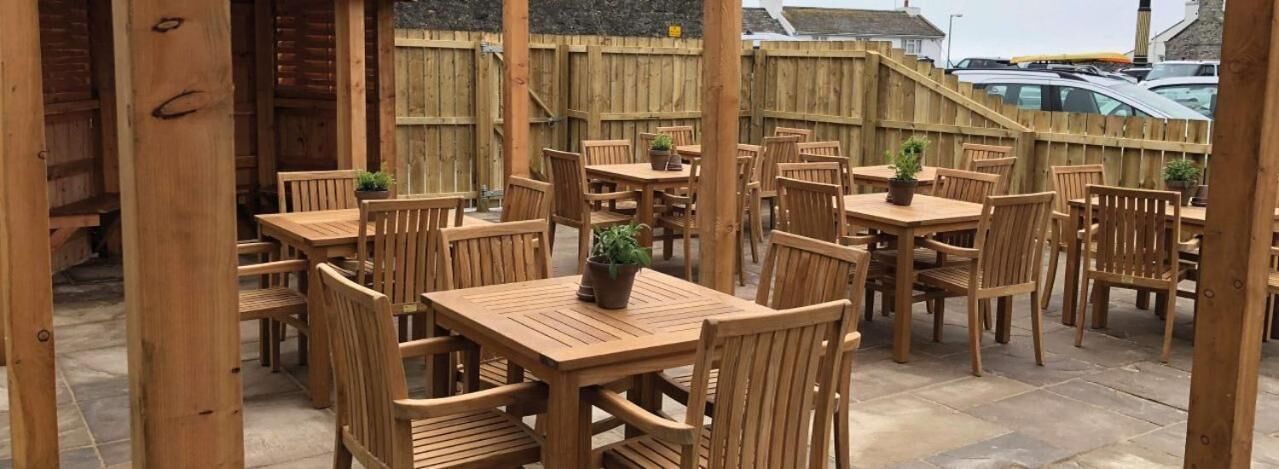 An outdoor patio with wooden tables and chairs, surrounded by a wooden fence.