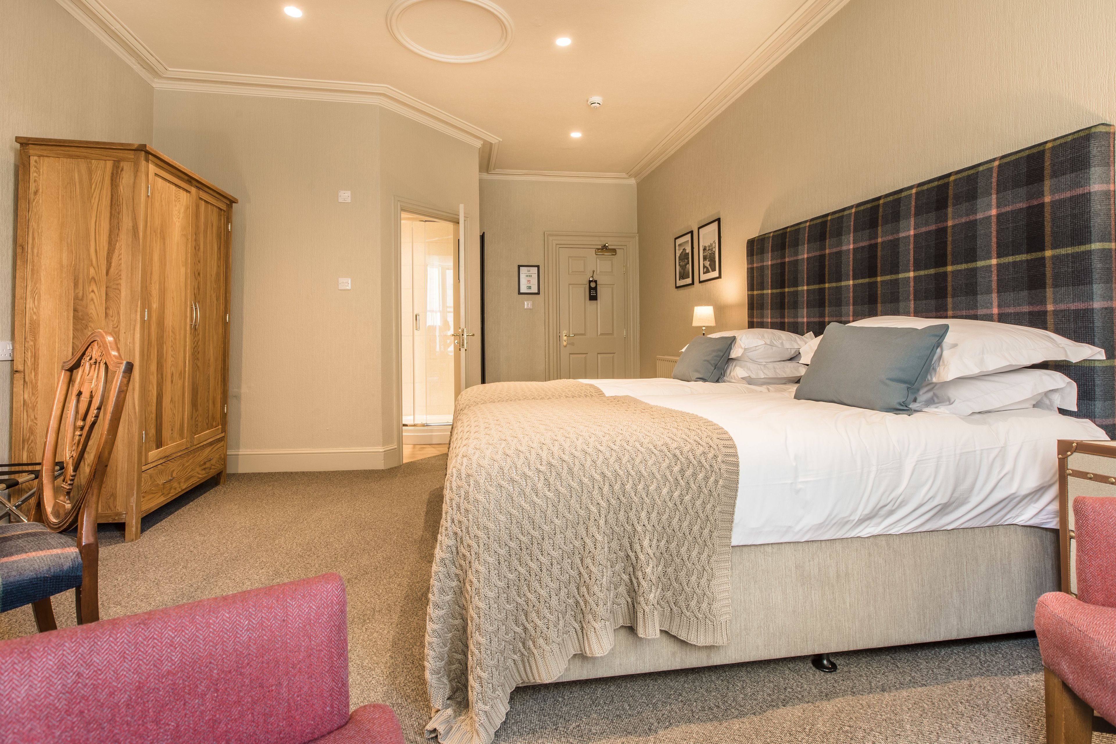 A bedroom with a large bed, a wardrobe, and two chairs.