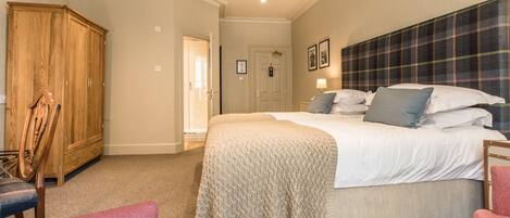 A bedroom with a large bed, a wardrobe, and two chairs.