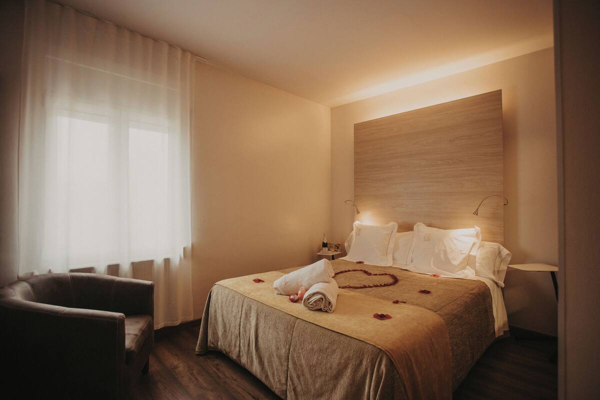 A hotel room with a bed, a chair, a bedside table, and a lamp.
