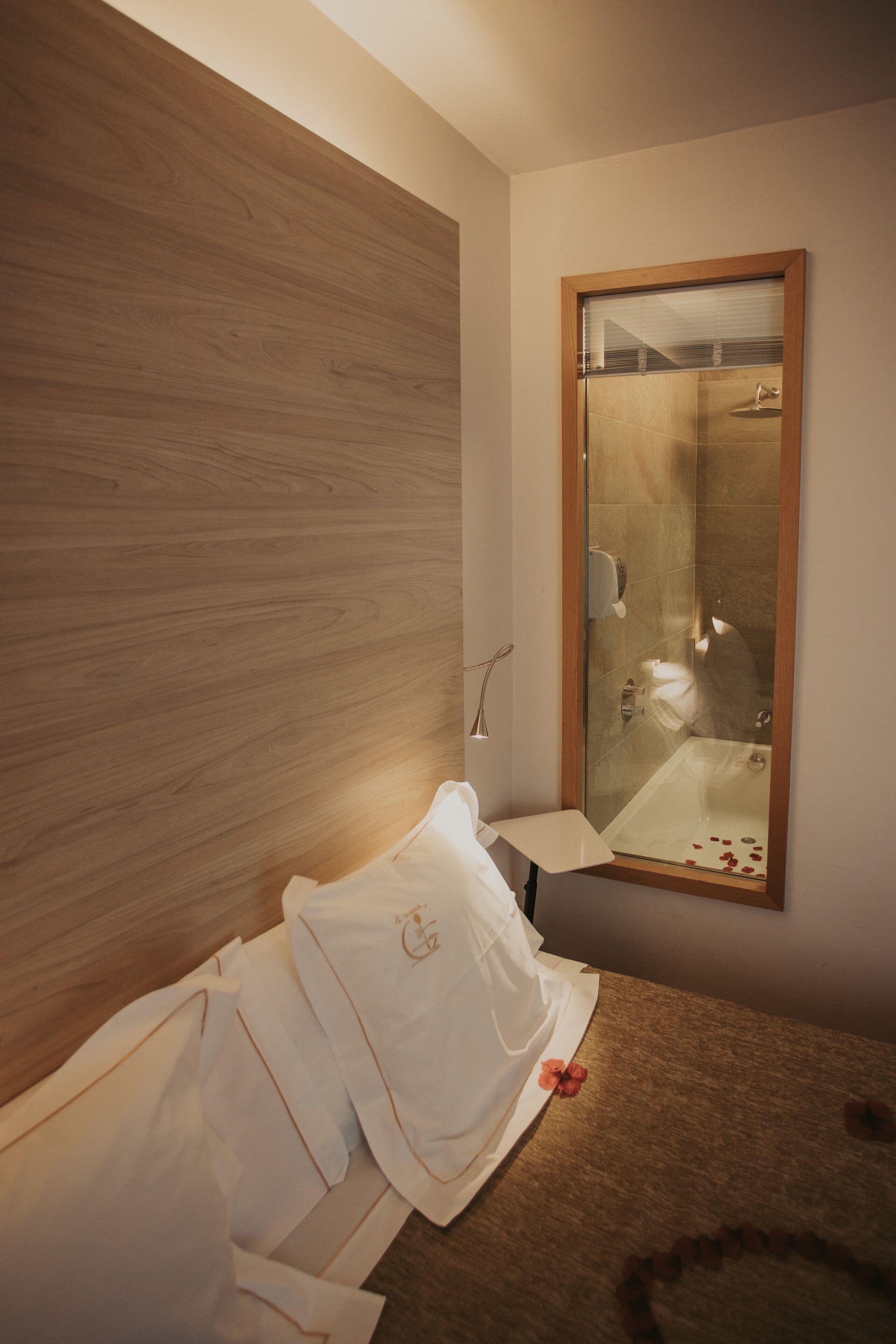 Una habitación de hotel con cabecera de madera, un espejo grande, una mesita de noche con lámpara y camas bien hechas.