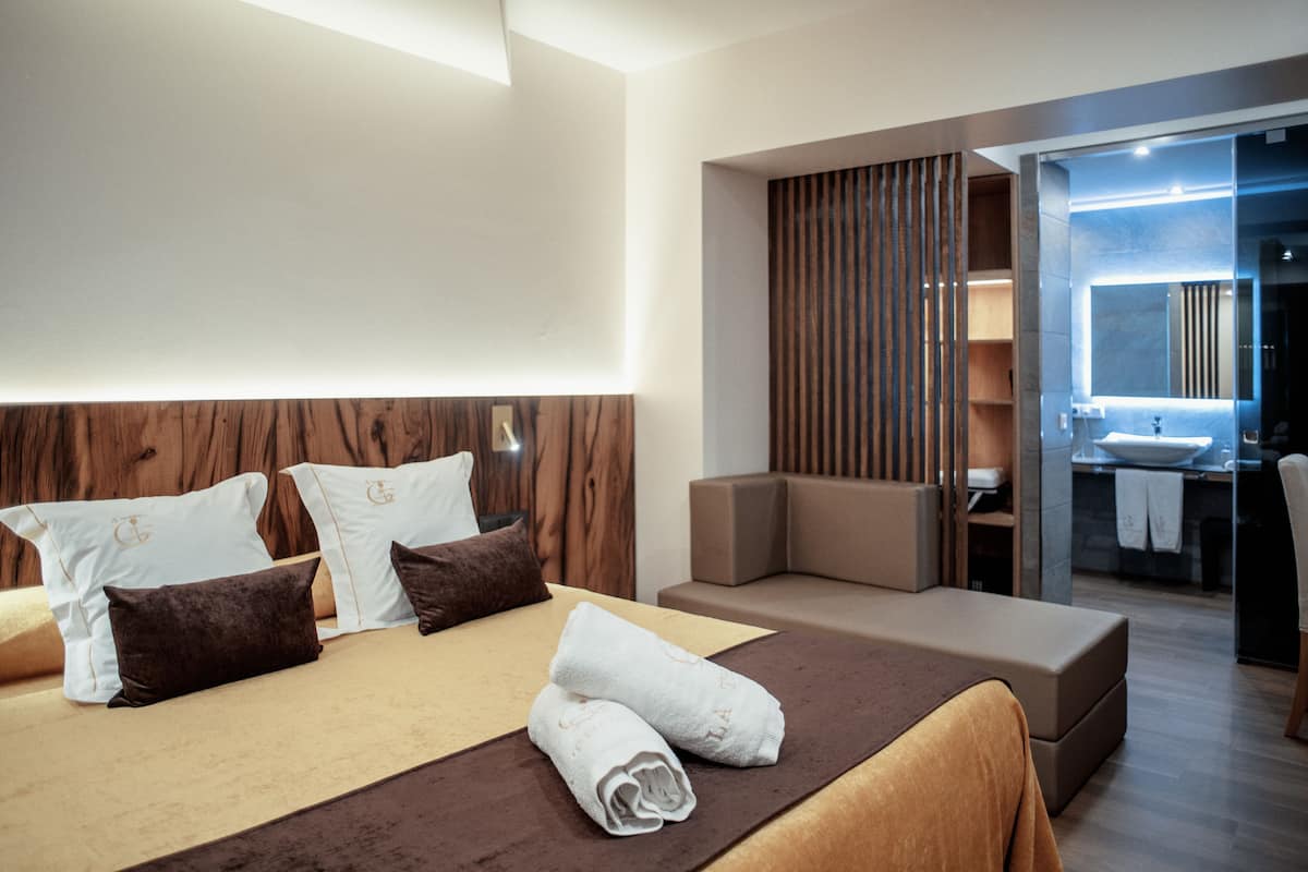 A modern hotel room with a large bed, a seating area, a bathroom with a large mirror, and a view into the bathroom.