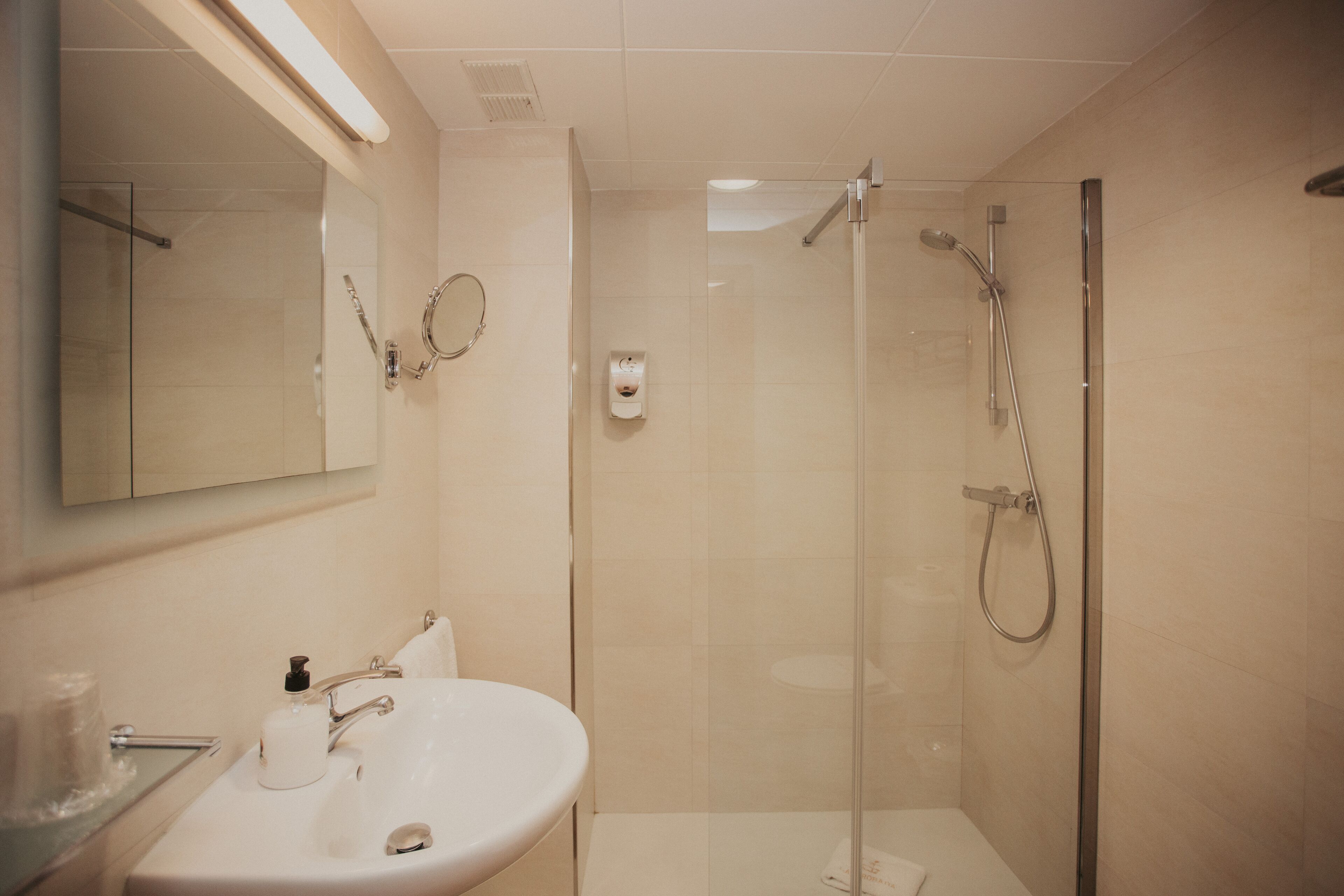 Un baño moderno con ducha de vidrio, un lavamanos blanco y un espejo sobre el lavamanos.