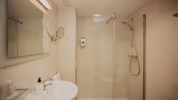Un baño moderno con ducha de vidrio, un lavamanos blanco y un espejo sobre el lavamanos.
