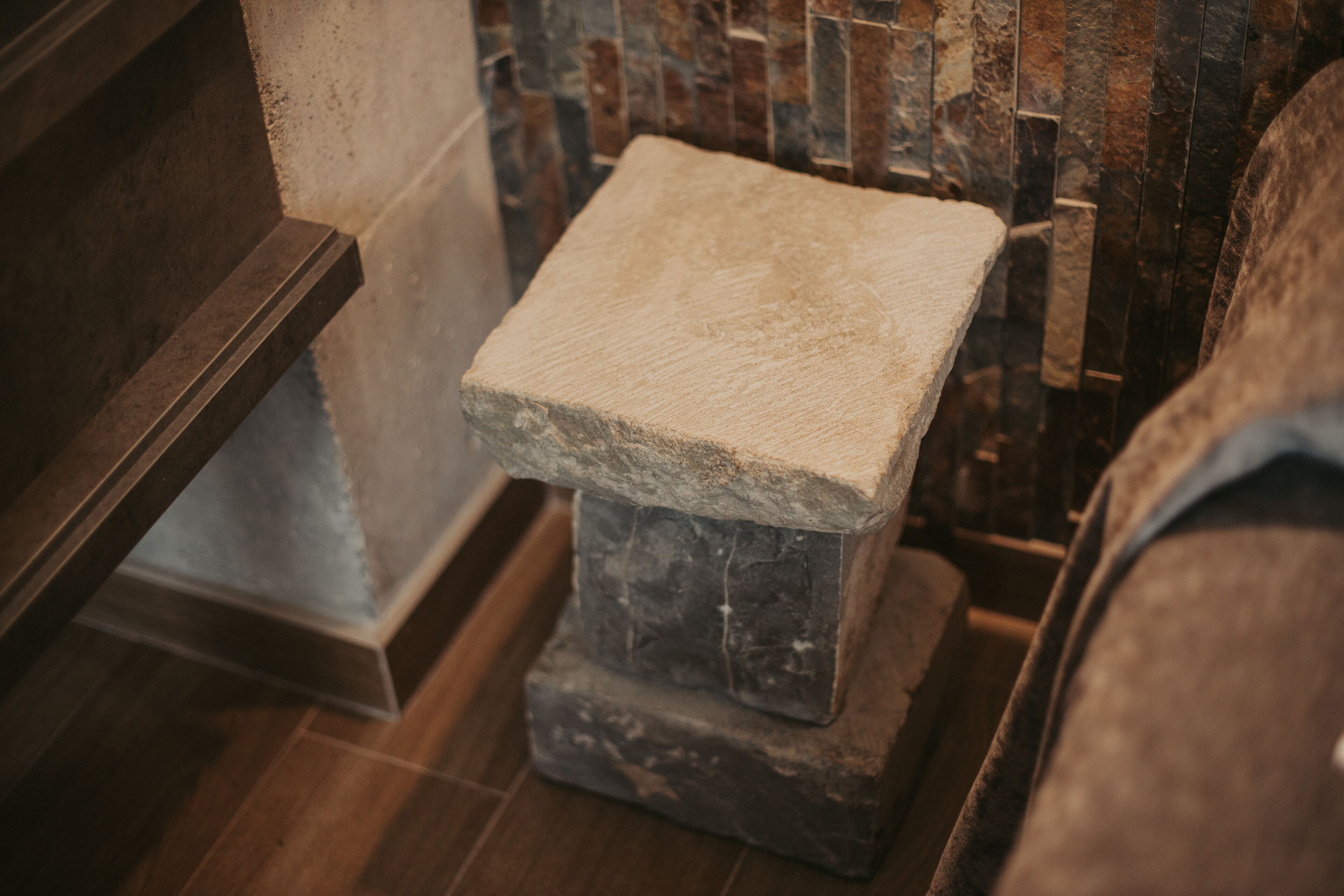 A stone bench with a rough texture, positioned in a corner with a wooden floor and a stone wall in the background.