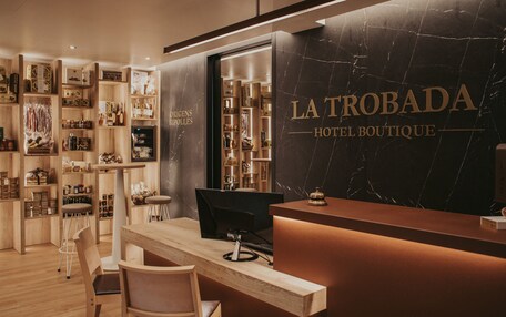 A hotel boutique interior with a reception desk, wooden shelves with various items, and a marble wall with the hotel name.
