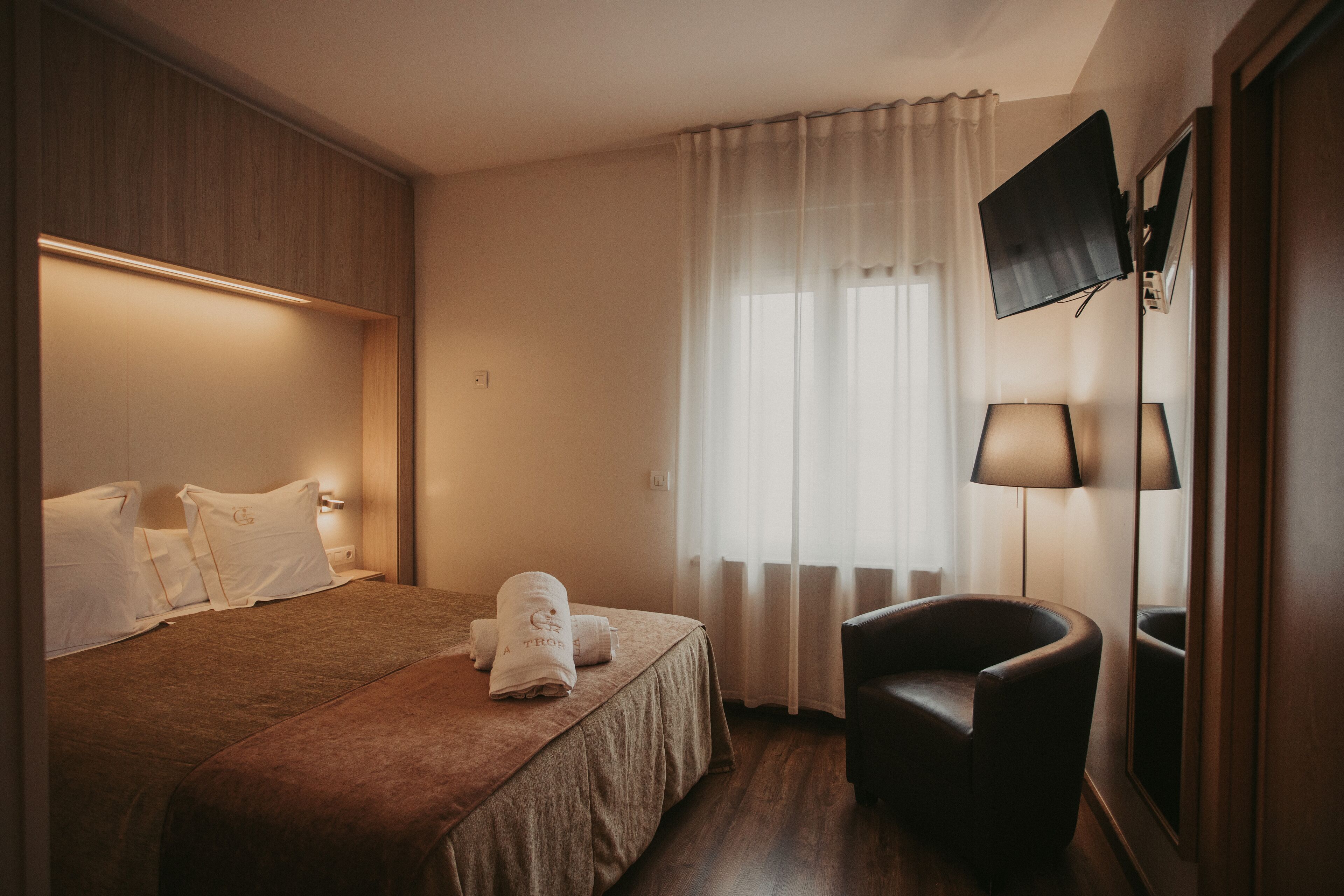 Une chambre d’hôtel avec un lit, une chaise, une télévision et une fenêtre avec des rideaux.