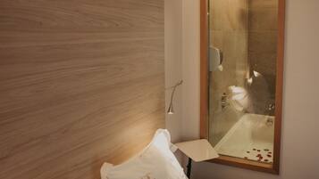 Une chambre d’hôtel avec une tête de lit en bois, une douche en verre, une table de chevet avec une lampe et des lits parfaitement faits.