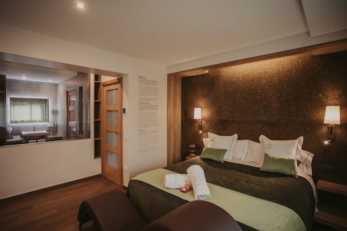 A hotel room with a large bed, a bedside table, a mirror, and a wall-mounted information board.