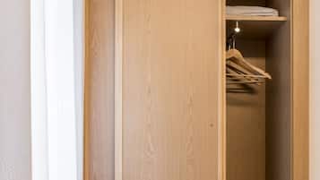Un armario de madera con espacio para colgar, una cama con manta color beige y suelo de madera.