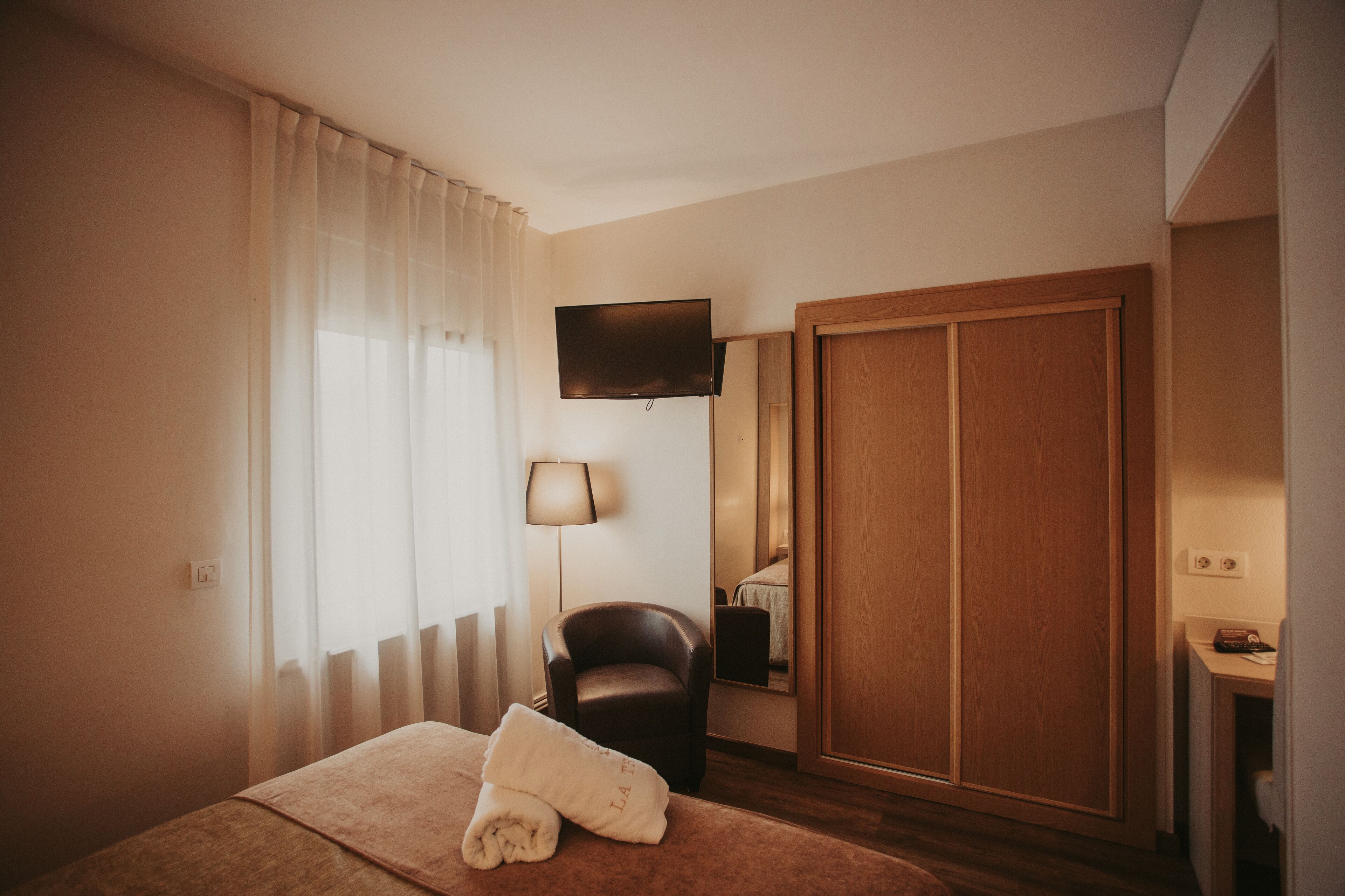 Una habitación de hotel con una cama, una silla, un televisor, un armario y una lámpara.