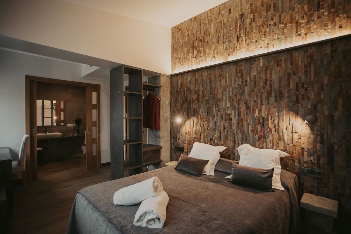 A modern bedroom with a large bed, a wooden textured wall, and a built-in wardrobe.