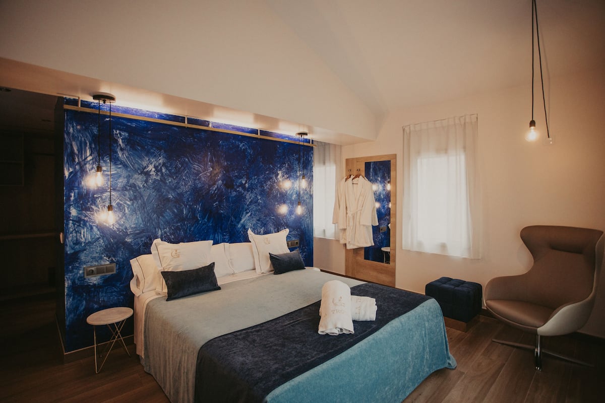 A modern bedroom with a large bed, a side table, a chair, and a wall with a blue abstract design.