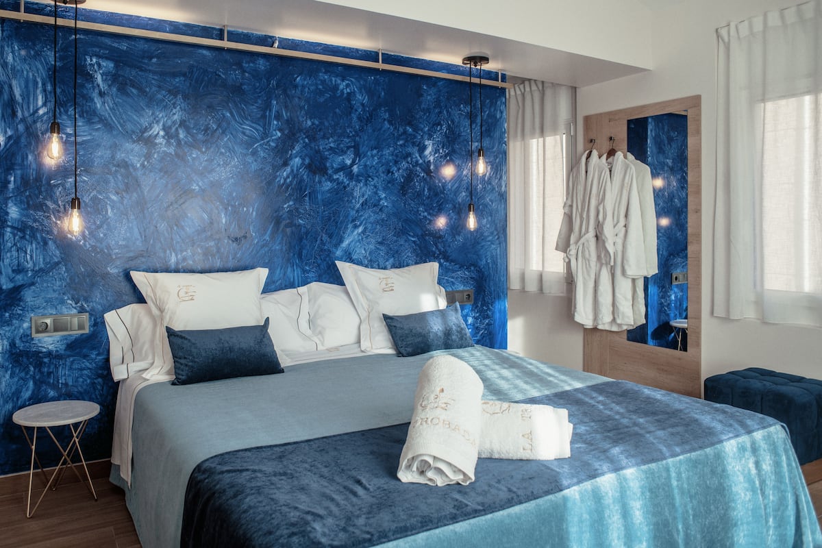 A modern bedroom with a large bed, a small side table, and a mirror with a robe hanging.