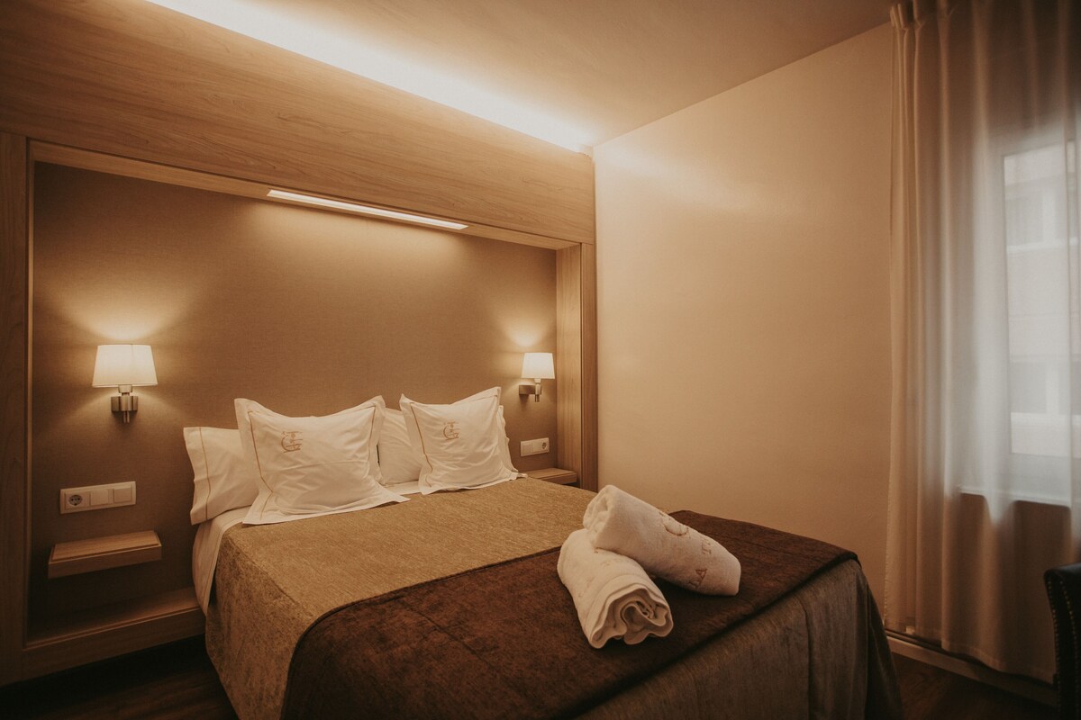 A hotel room with a large bed, two bedside lamps, a nightstand, and a window with curtains.