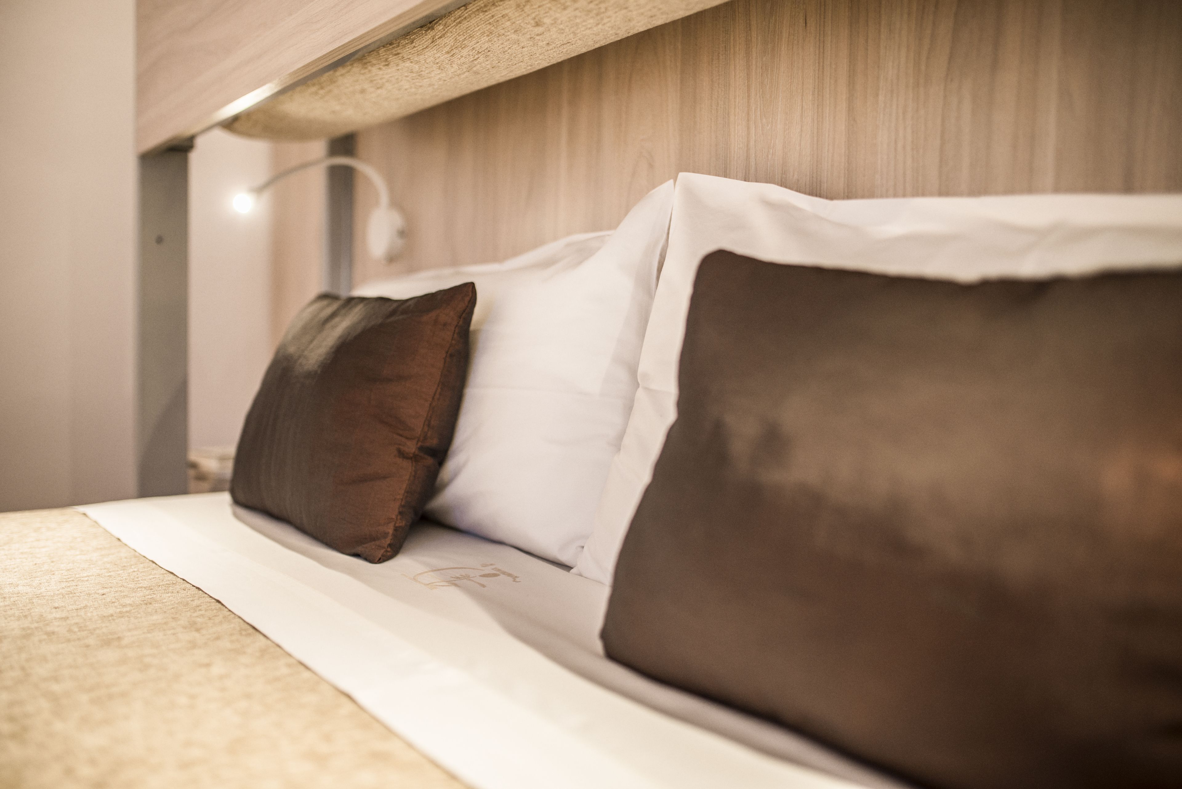 Una cama con almohadas blancas y marrones, un cabecero de madera y una lámpara sobre ella.