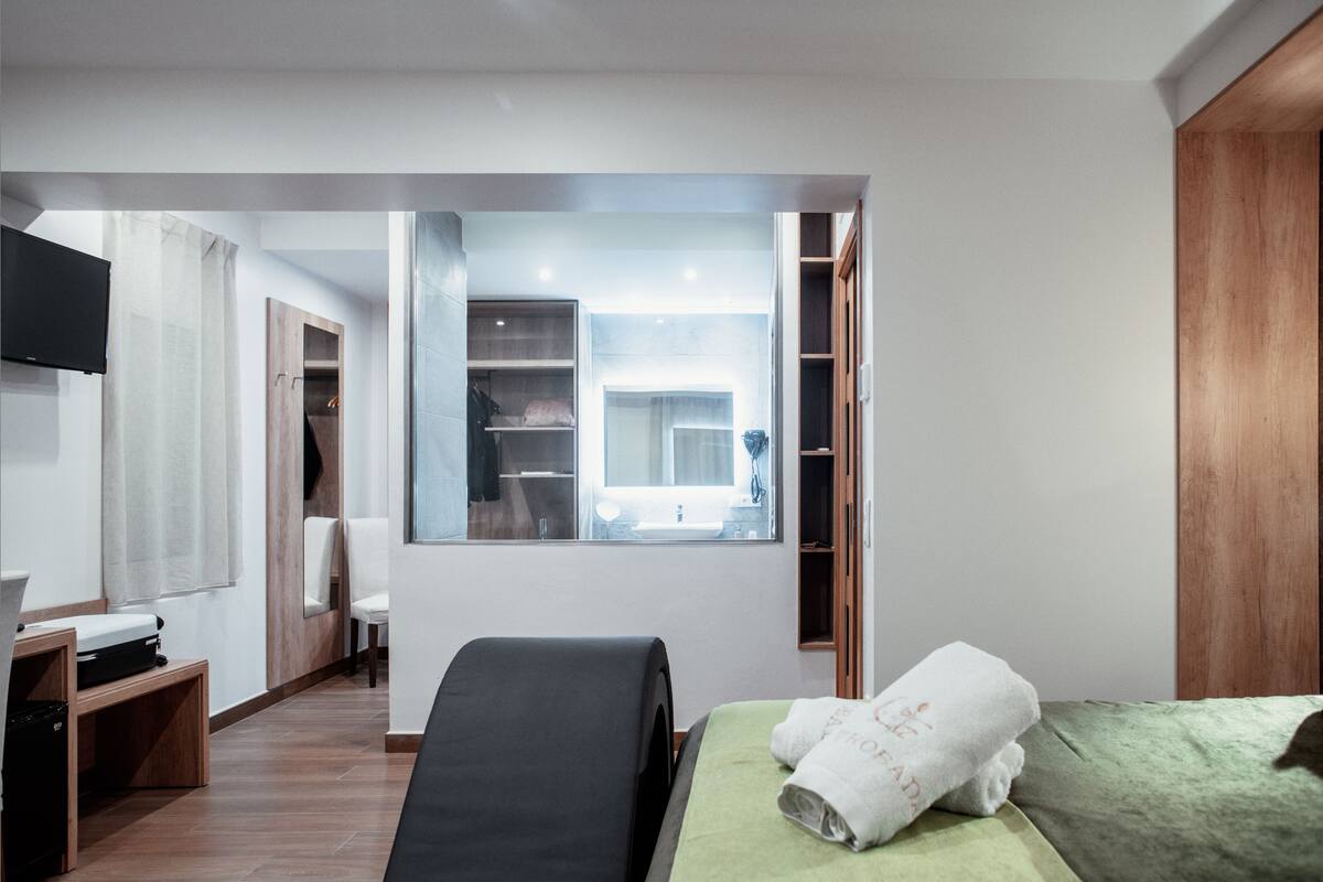 A modern hotel room with a bed, a desk, a chair, a TV, and a large window.