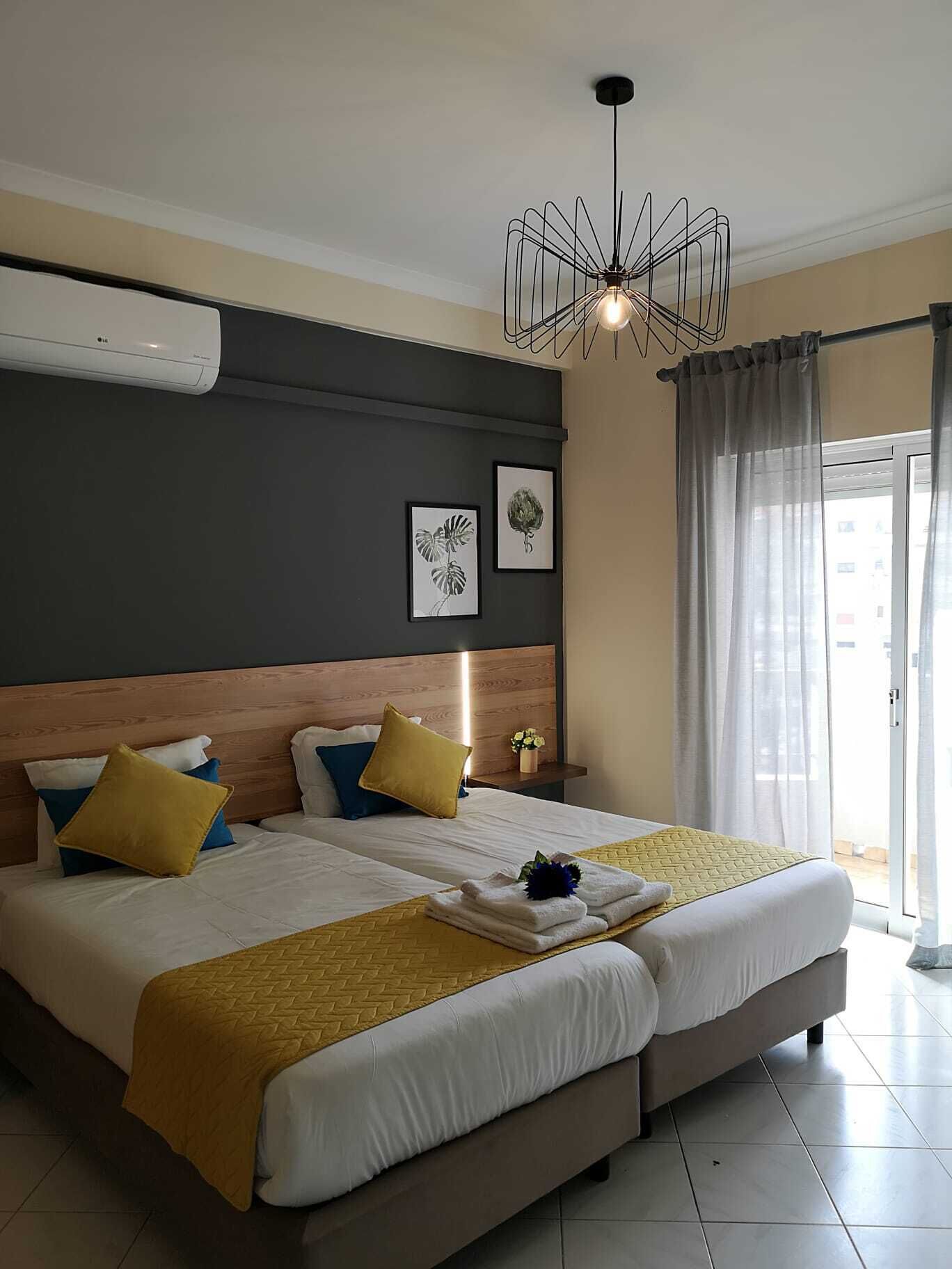 Une chambre d’hôtel avec un grand lit, un lustre moderne et une vue par la fenêtre, qui est ornée de rideaux.