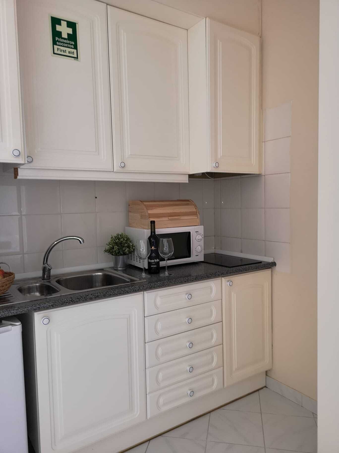 Cucina con mobili bianchi, lavello, forno a microonde e un piccolo tagliere di legno.