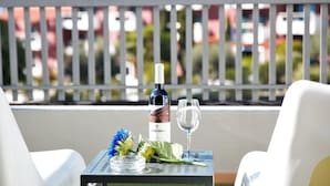 Ein Balkon mit Tisch für zwei Personen, ausgestattet mit einer Weinflasche, einem Glas und dekorativen Blumen.