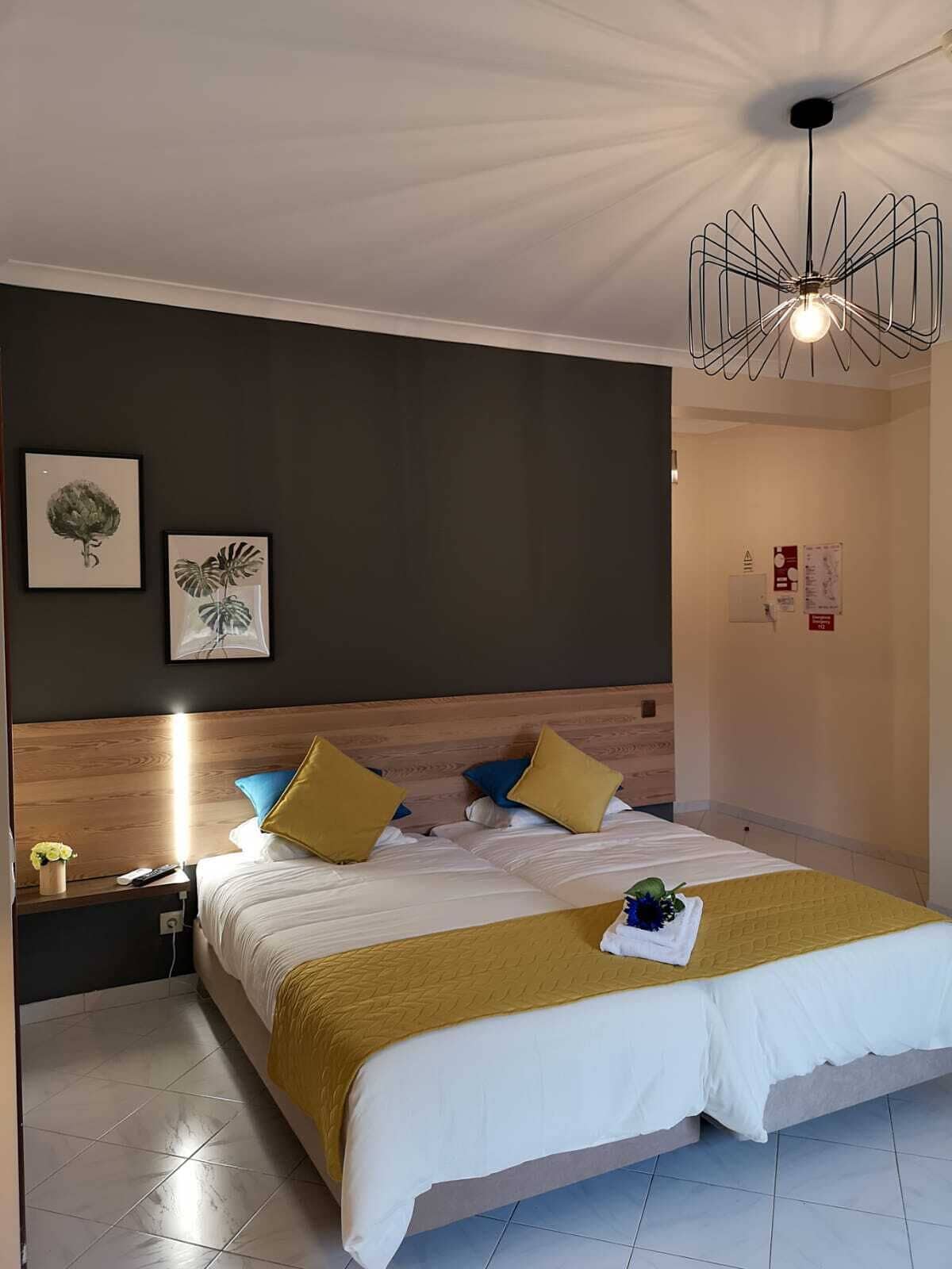 A modern hotel room with a large bed, wooden headboard, and a unique ceiling light fixture.