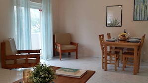 Ein Essbereich mit einem Holztisch, gedeckt für vier Personen, einer Bank und einem Stuhl. Auf dem Tisch steht ein Blumentopf und ein kleiner Tisch mit einem Buch und einer Kerze.