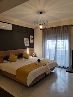 A modern hotel bedroom with a large bed, a ceiling light fixture, and a window with curtains. - Kiss Apartamentos (Albufeira)