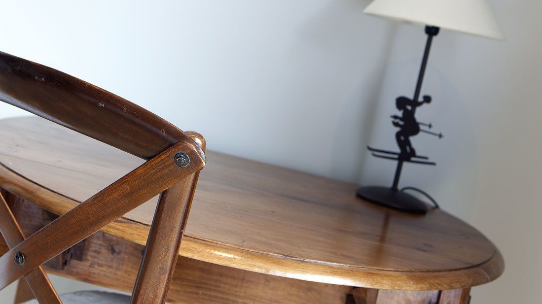 Una silla de madera con bisagra metálica y una mesa redonda de madera con una lámpara.