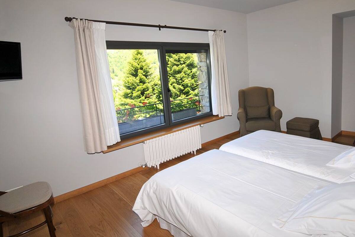 A bedroom with a large bed, a chair, a desk, and a window with curtains.