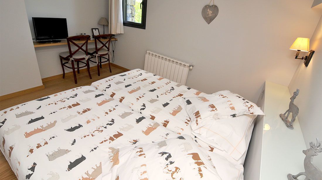 A bedroom with a bed, a desk with a TV, chairs, a radiator, and decorative wall art.