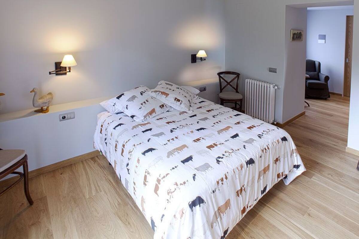 A bedroom with a bed, two wall-mounted lamps, a chair, a radiator, and a mirror.