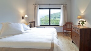 A bedroom with a large bed, a wooden dresser, a chair, and a window with a view of greenery. - L'Hotelet del Bac (Camprodon)