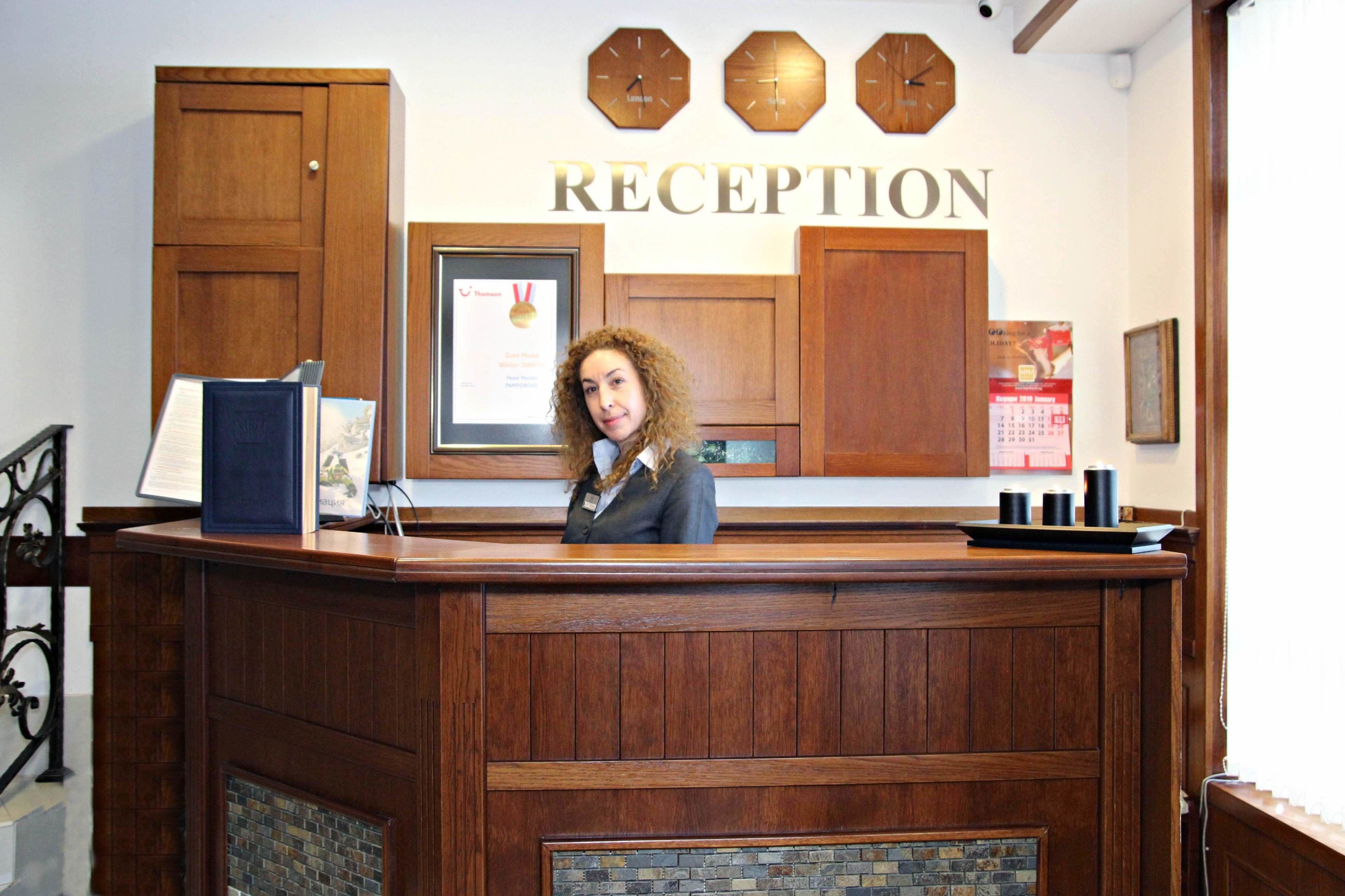 A reception desk with a framed certificate, wooden cabinets, and a clock above the word "RECEPTION" on the wall.