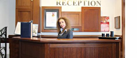 A reception desk with a framed certificate, wooden cabinets, and a clock above the word "RECEPTION" on the wall.