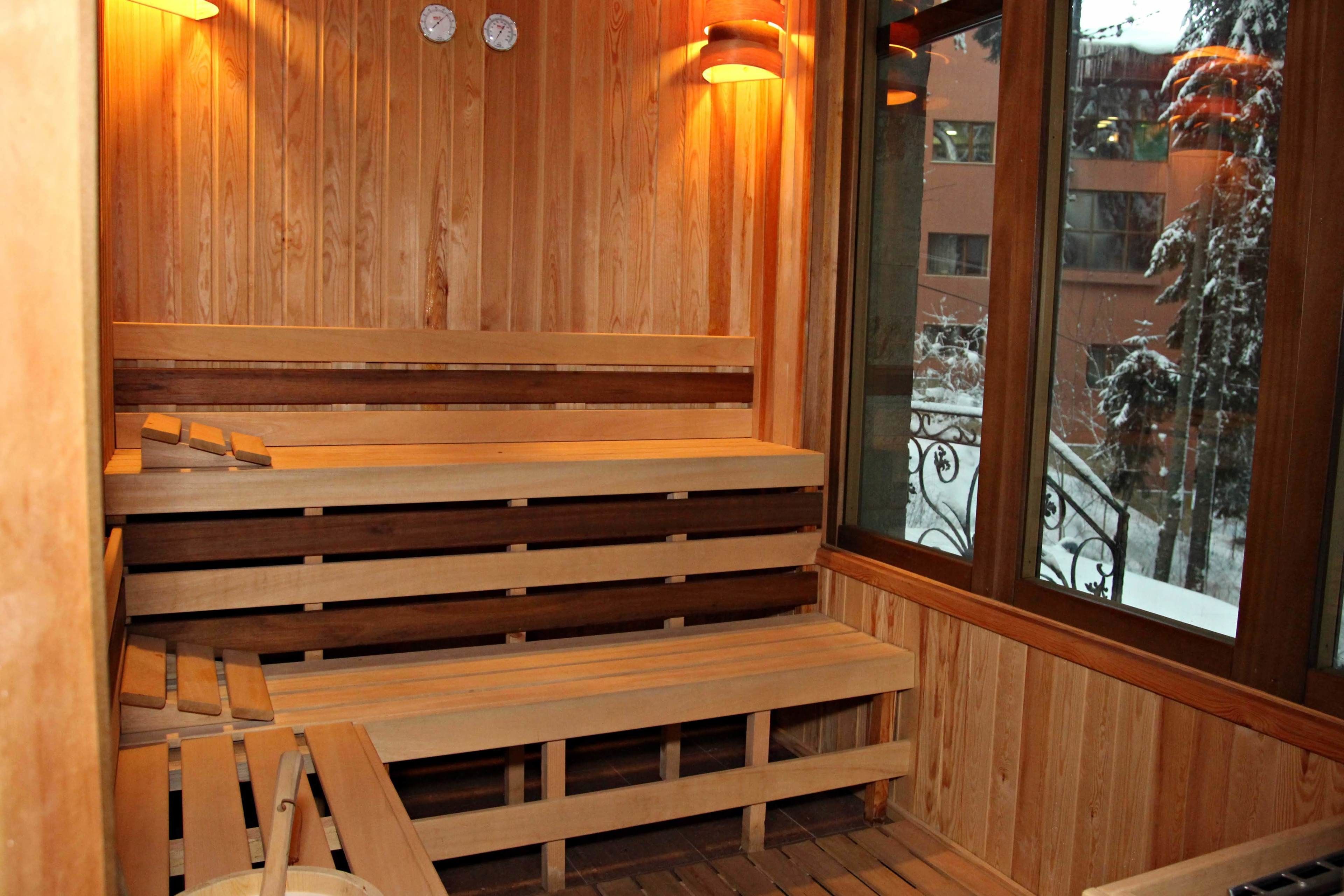 A wooden sauna with benches and a window overlooking a snowy cityscape.