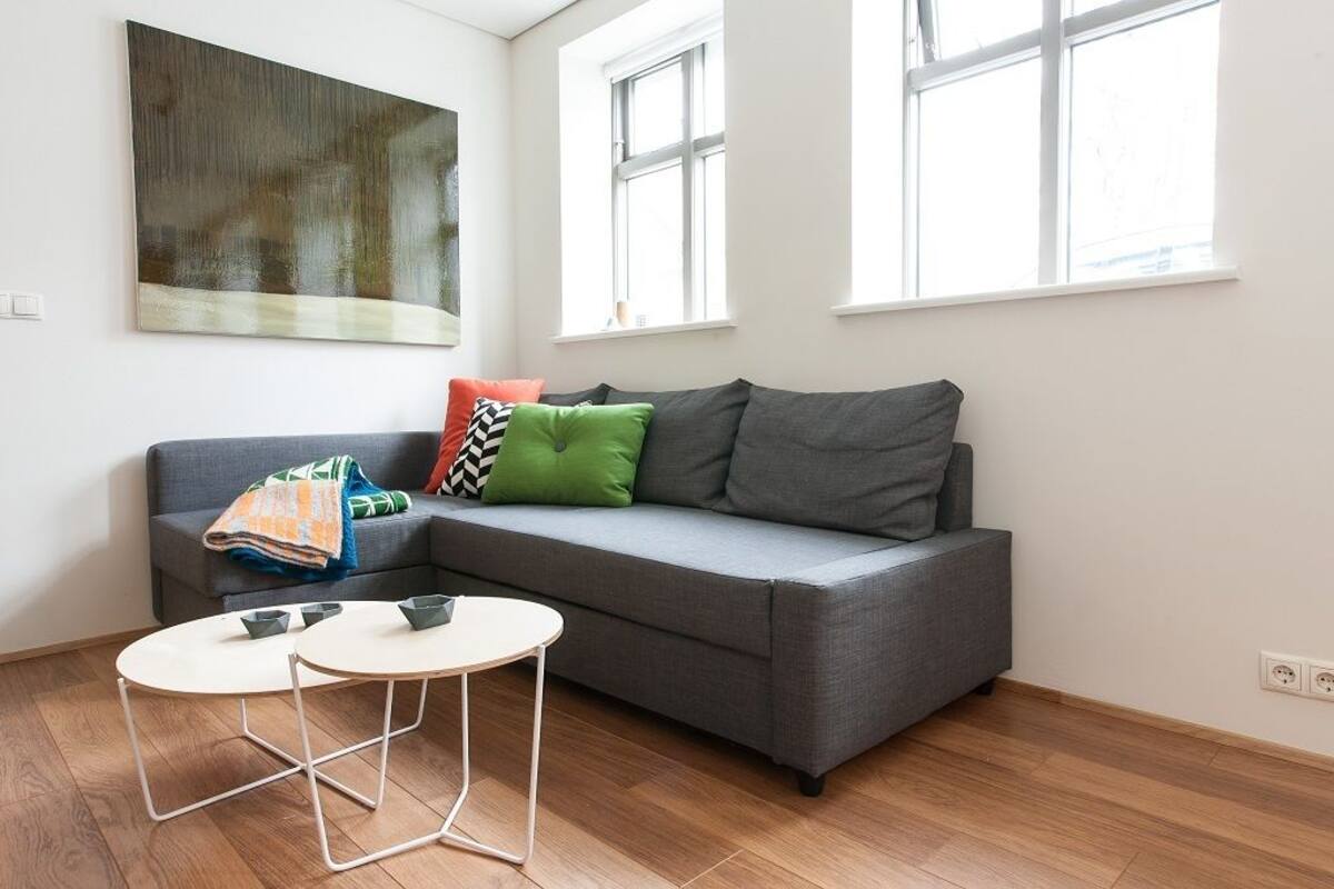 A modern living room with a grey sofa, colorful cushions, a small white table, and a large abstract painting on the wall.