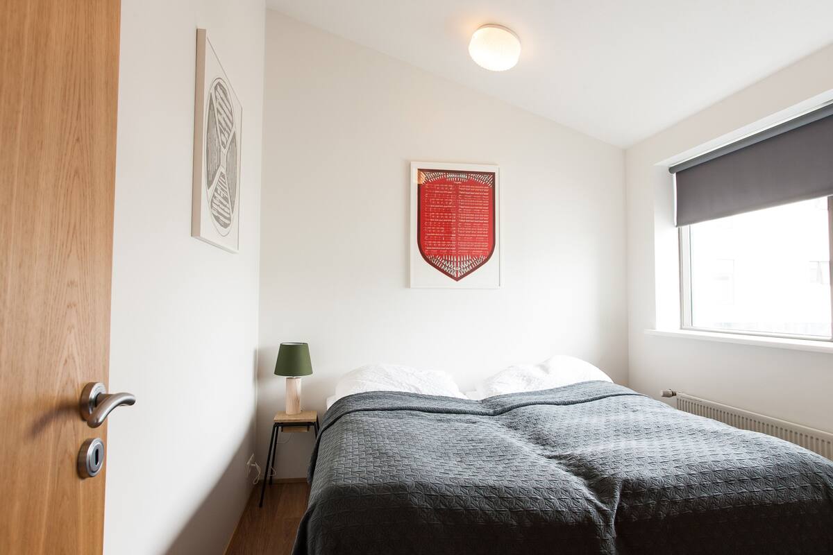 A bedroom with a bed, a nightstand, a lamp, and two wall art pieces.