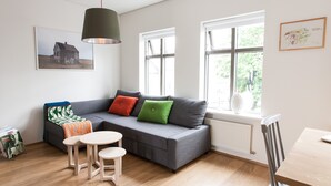 A modern living room with a grey sofa, two small round tables, and a window with a view of trees. - Mengi Apartments (Reykjavik)