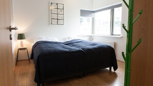 A bedroom with a bed, a standing lamp, a window, and a radiator. - Mengi Apartments (Reykjavik)
